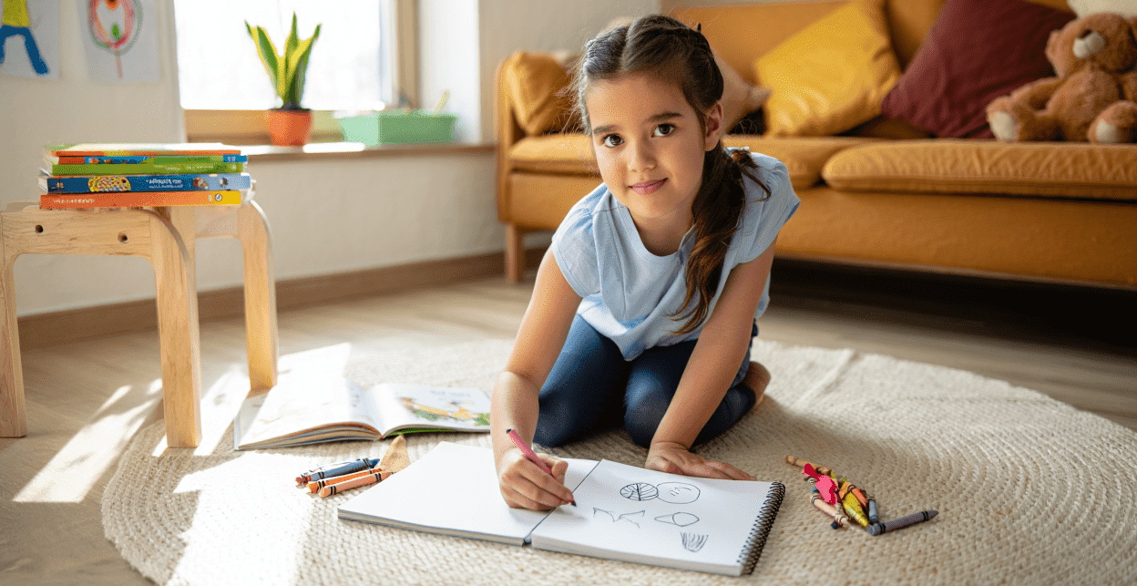 Child drawing in a sketchbook on the floor with crayons.